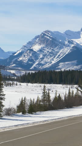 SLOW MOTION: Scenic view of the snowy Canadian Rockies as car disappears in the distance. Driving along the famous Icefields Parkway tourist route on sunny winter day. Picturesque Banff National Park