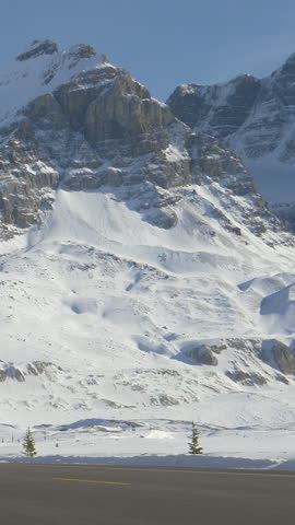 ICEFIELDS PARKWAY, ALBERTA, CANADA, MARCH 3, 2019: LOW ANGLE: Car drive towards a spectacular snowy mountain in the beautiful Canadian Rockies. Tourists explore the famous Icefields Parkway route.