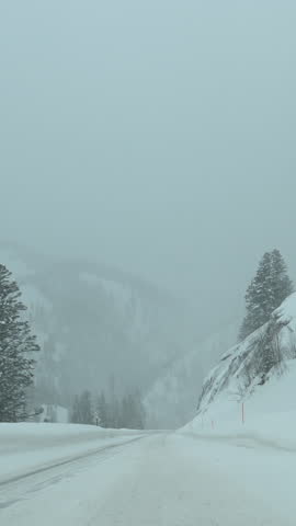 POV Scenic view of driving down the snowy asphalt road leading toward Teton Pass. Wintry mountain landscape surrounds the famous interstate highway running across the states of Wyoming and Idaho.