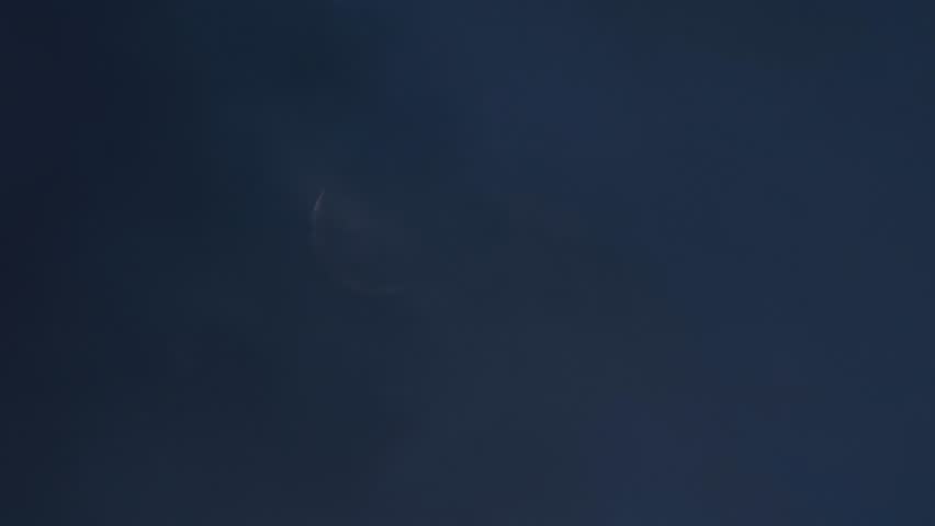 A Crescent moon gradually appearing behind faint Moving clouds at dawn
