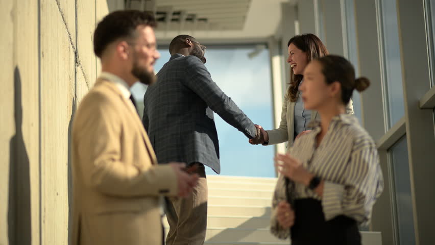 Professional business partners exchanging firm handshake, celebrating successful negotiation inside bright, modern corporate office building with confident, positive body language