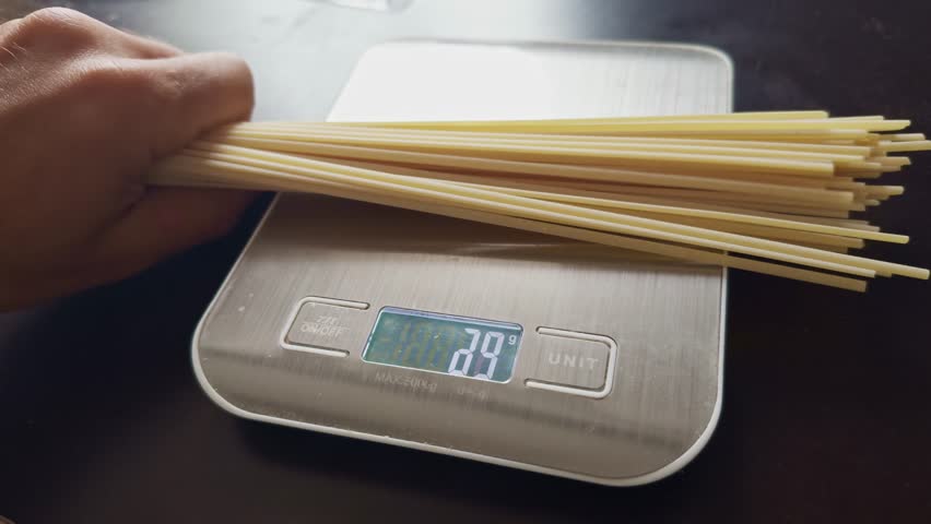Balanced diet. Uncooked spaghetti being weighed on digital kitchen scale. Dieting loose weight pasta portion. Precise cooking and portion control on dieting. Healthy cooking gluten free pasta on diet