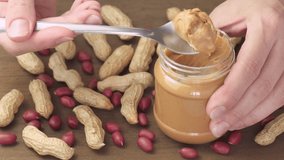 Female hands taking a spoon of tasty peanut butter from a jar. Macro shot. Groundnut on wooden table. Sweet organic food. - Powered by Shutterstock - Get 15% off with code: PIKWIZARD15