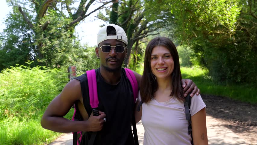 Young multi ethnic couple wearing backpacks and posing for snapshots while hiking on a sunny day