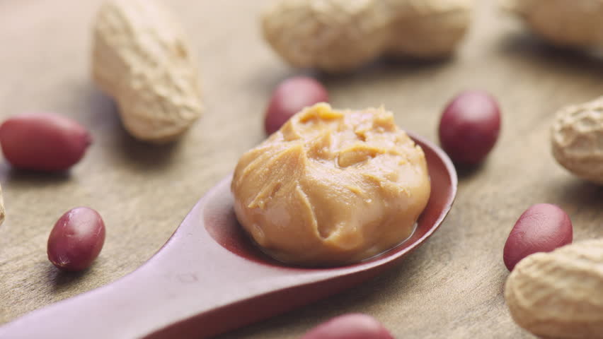 Wooden spoon of tasty peanut butter. Macro shot. Groundnut on wooden table. Sweet organic food.