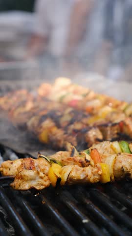 Vertical video of a grill master cooking shashlik with pieces of meat vegetables and spices over open flames outdoors. Street meat food with great taste and aroma. Hot delicious grilled meat.
