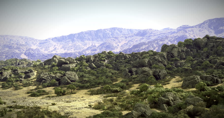A stunning rocky landscape featuring large boulders scattered across the terrain, with green vegetation dotting the ground and majestic mountains in the background under clear skies.