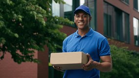 Smiling African American ethnic courier portrait standing in city smile looking at camera delivery man male guy post worker holding parcel postal order shopping service work deliver in blue uniform - Powered by Shutterstock - Get 15% off with code: PIKWIZARD15