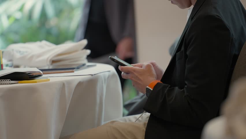 Close-up of Businessman Hands Typing on Mobile Phone in Meeting Room