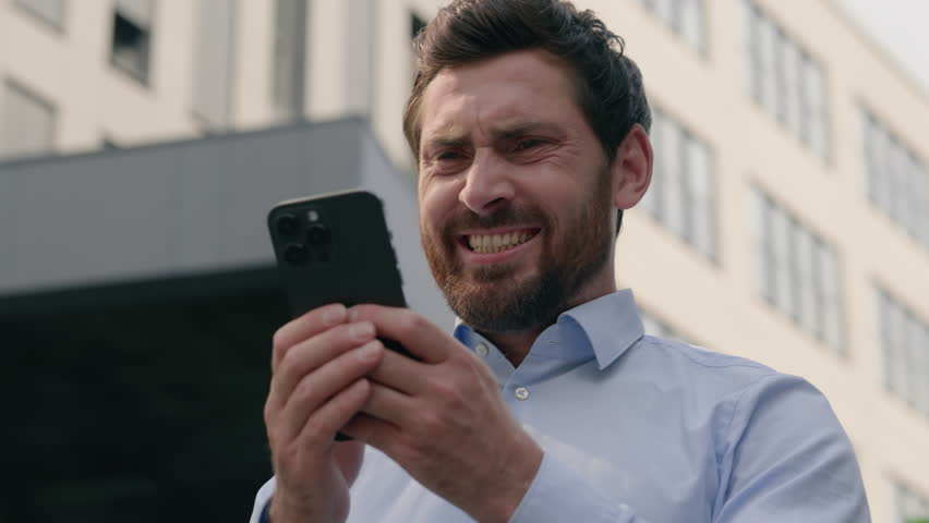 Angry irritated annoyed stressed Caucasian middle-aged businessman business man male guy entrepreneur in city near office building using mobile phone app chatting smartphone message work job problem