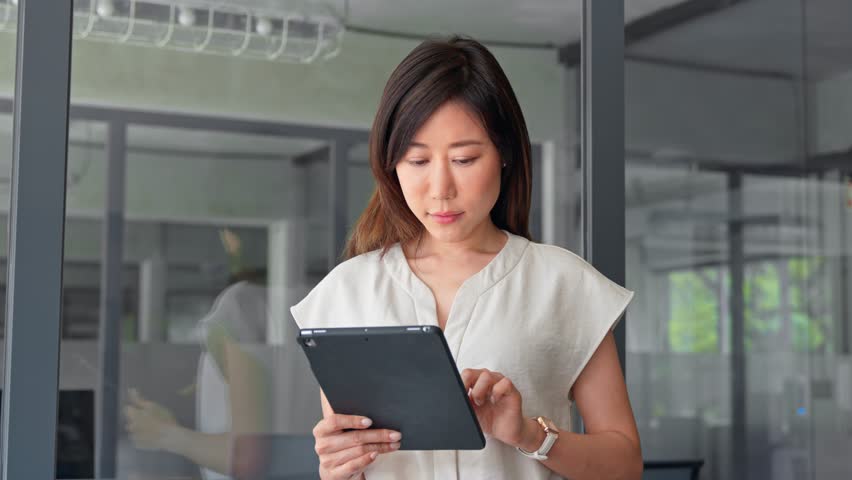 Smiling ceo entrepreneur businesswoman leader using touchscreen pc device in office. Asian middle-aged woman using tablet reading news browsing, doing online work, business learning or communication. 