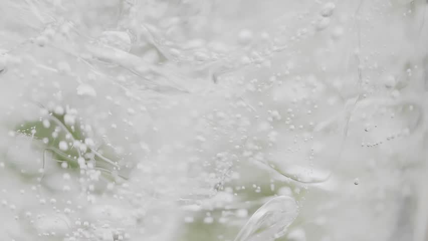 Super slow motion footage: Carbonated water being poured into a glass filled with ice in the summer outdoors