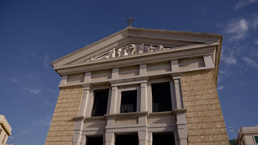 Low angle view of Sanctuary of Maria Santissima Immacolata in Scilla, Calabria, Italy, highlighting architectural details, statues, and cross against vibrant blue sky