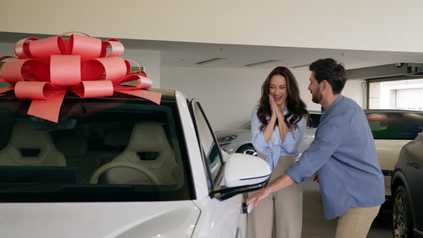 Happy Caucasian family buying new car man open door present gift automobile to lovely woman surprise excited sitting inside auto test drive couple love choose transport in salon showroom rent service