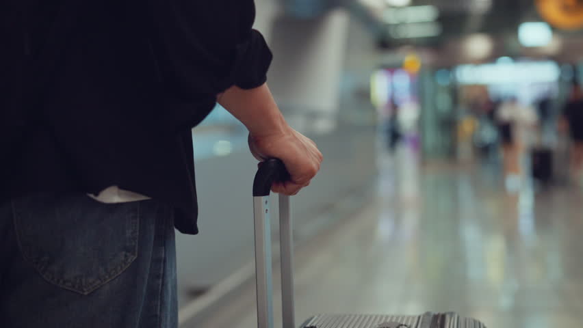 Rear view - Male traveler walking with luggage or suitcase at the modern airport terminal, man on way to flight boarding gate, Ready for travel or vacation journey
