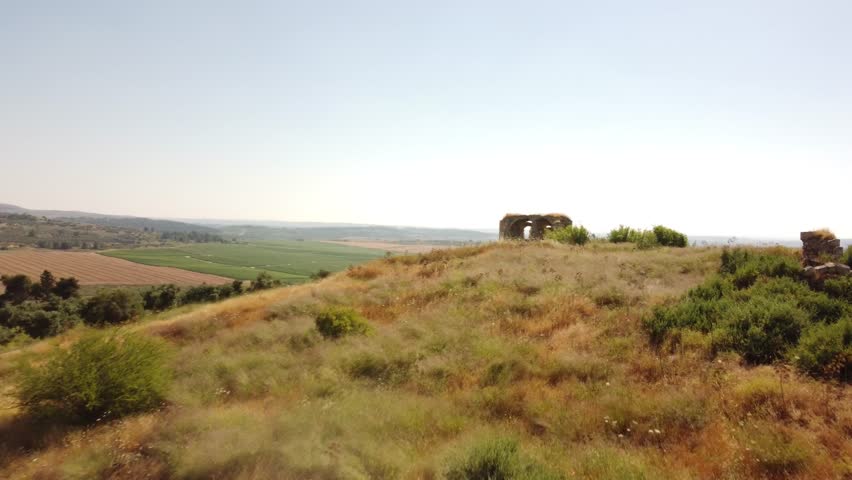 Discover the serene beauty of Israel, showcasing an ancient arch set amidst vast agricultural fields under a clear sky.