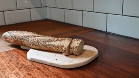Close-up of a woman's hands slicing fresh, crusty seeded baguette bread on a rustic wooden cutting board in a modern kitchen. - Powered by Shutterstock - Get 15% off with code: PIKWIZARD15