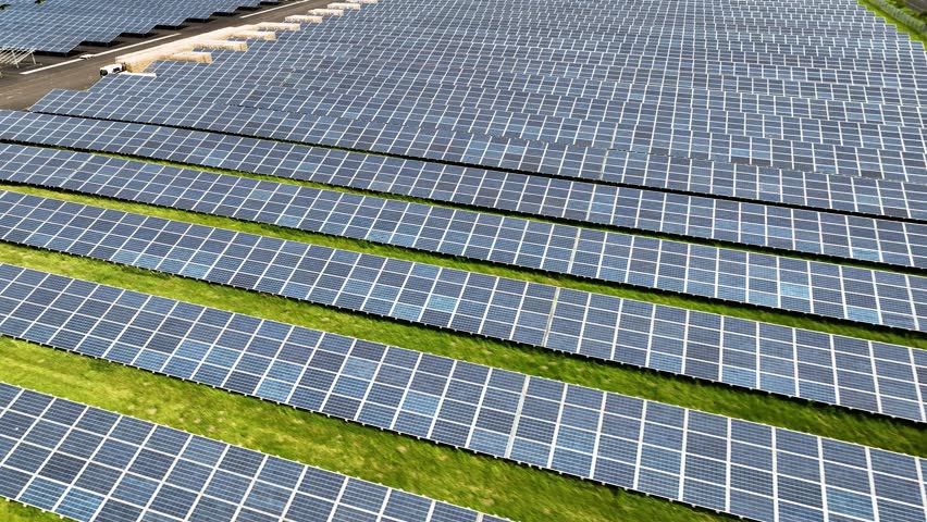 Aerial footage of large-scale solar farm under construction with thousands of photovoltaic panels, trucks and equipment on-site indicate ongoing construction or maintenance, pallets on site. 