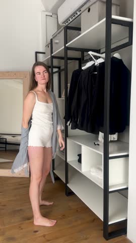 Sad woman in bathrobe and pajamas throw clothes from the closet on floor in bedroom. Displeased with old clothes choosing. Woman's mental health and everyday problems. Upset with life challenges.