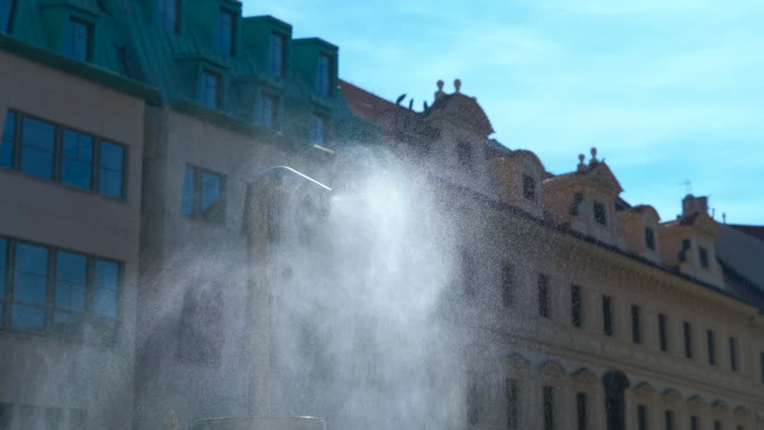 Water vapor sprinkler refreshing city street during hot summer day. Vapor cloud billowing from urban street sprinkler, dispersing cooling mist and lowering ambient temperature during summer heat wave