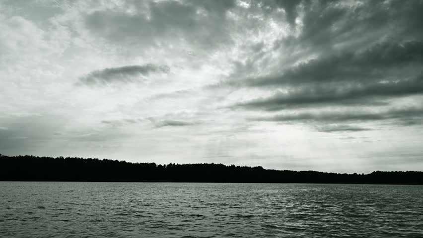 Lake and cloudy sky at sunset from the deck of a sailing boat, black and white 