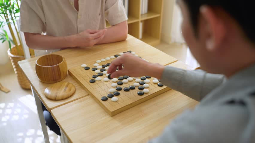 Close up of young men play board game Go during competition in community. Attractive two male friend players participate in traditional asian chinese board game match on table in the club house center