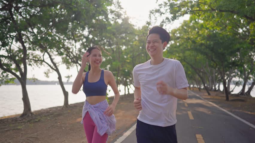 Asian young couple doing running exercise in the morning outdoors garden. Attractive man and woman feel happy and relax, spend their romantic day jogging side by side through a beautiful garden path.