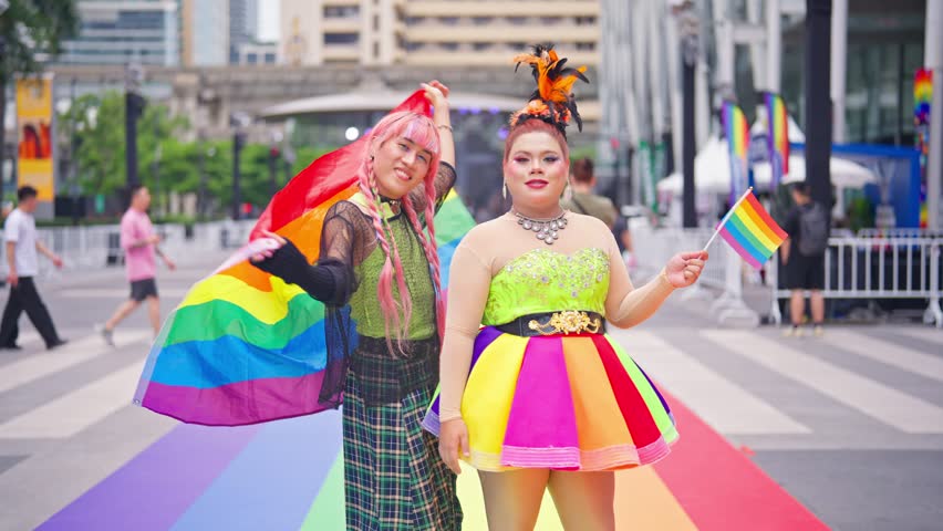 Portrait of confident LGBTQ people posing proudly during Pride Month. Young transgender women holding rainbow flags, spend time outdoors in city streets, celebrating identity and diversity together.