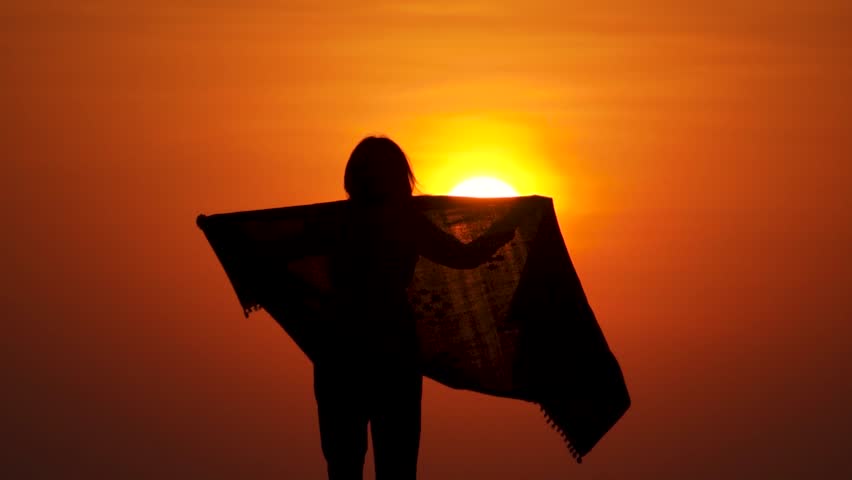 Silhouette of teen girl with open arms in sunset against orange sun. Girl enjoying sunlight. Carefree person living a free life. Success freedom happy life concept. Tourist enjoying sunset views.