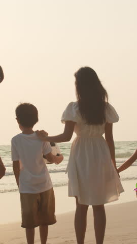 Vertical Screen : Asian young happy family enjoy vacation on beach in evening. Dad, mom and kid relax walking together near sea when sunset. Lifestyle travel holiday vacation summer trip. Slow motion.