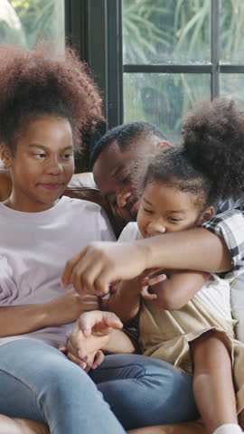 Vertical Screen : Happy cheerful African American family dad and daughter having fun cuddle play on sofa while birthday at house. Self-isolation, stay at home, social distancing for prevention.