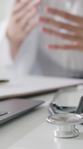 Vertical Screen : Young Asia lady doctor in white medical uniform with stethoscope using computer laptop talking video conference call with patient at desk in hospital. Consulting and therapy concept.