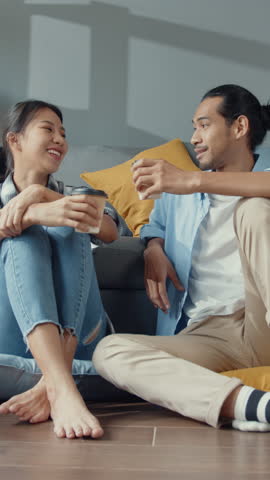 Vertical Screen : Happy asian young attractive couple man and woman sit at new home drink coffee relax and talk smile with carton package box storage to move in new house. Married move home concept.