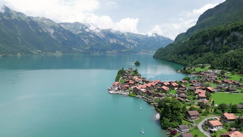 Flying over Iseltwalt at the turquoise lake Brienzer See near Interlaken in Switzerland surrounded by the alp mointains on a cloudy sunny day in the summer