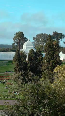 People relax and enjoy the day in front of the Conservatory of Flowers in Golden Gate Park, San Francisco, USA. Visitors are picnicking and walking.