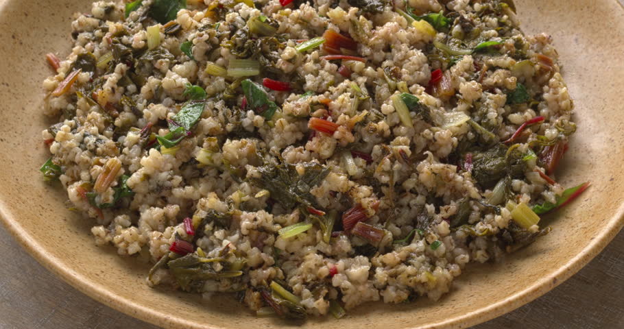 Barley groats with braised chard, seasoned with allspice on a plate. Table spin.