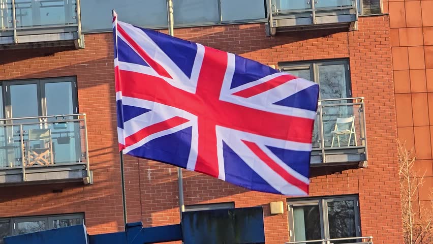 Medium shot of flag of the United Kingdom waving in the wind in front of a building during the day, outdoor