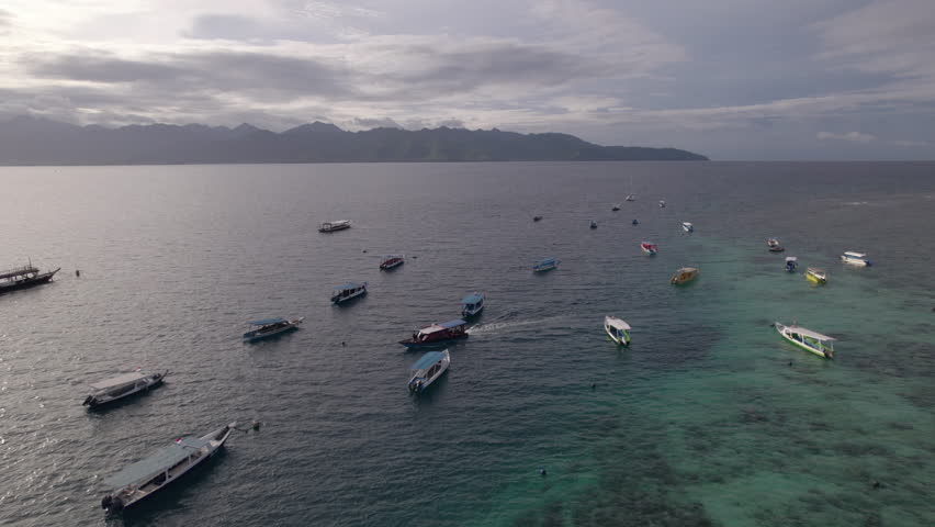 Aerial view tracking moving boat through moored vessels, Gili Trawangan, sunset