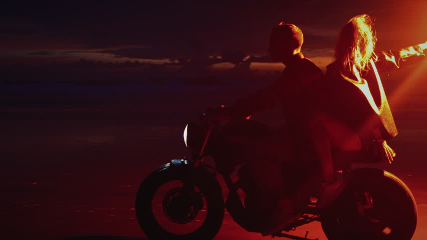Romantic woman and man ride on moto bike, Bali Indonesia asia, twilling sunrise. Two young couples riding on vintage motorcycles with red burning signal flares after sunset on beach, slow motion fire