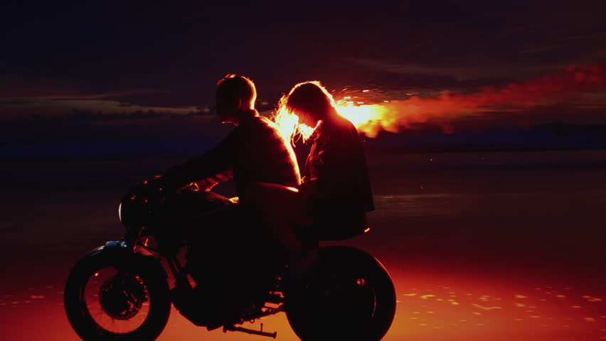 Romantic woman and man ride on moto bike, Bali Indonesia asia, twilling sunrise. Two young couples riding on vintage motorcycles with red burning signal flares after sunset on beach, slow motion fire