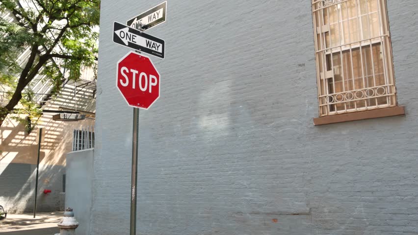 New York City oneway crossroad, Minetta street intersection one way arrow. Manhattan Greenwich Village residential building architecture, NYC United States. Blue brick wall, window, red stop road sign