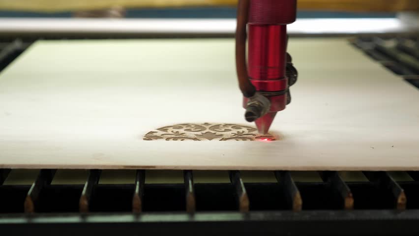 A close-up of a laser wood cutting machine cuts a particle board, and smoke appears. Laser beam for high-precision cutting of plywood sheet. Modern wood cutting technology.