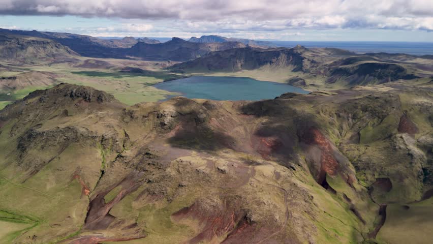 Aerial approaching shot of lake is Heidarvatn near Vík on the south coast of Iceland. Wide shot. Sunny day with blue sky and green hills.