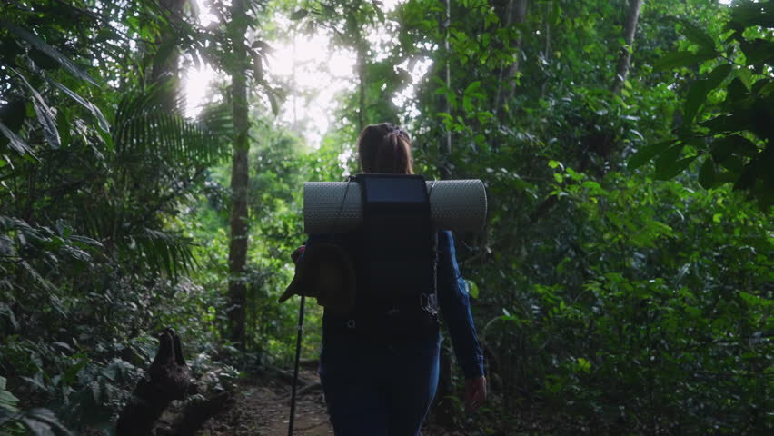 An Asian woman hikes through nature with a backpack equipped with a solar panel charger — representing sustainable trekking, off-grid adventure, and eco-friendly travel.
