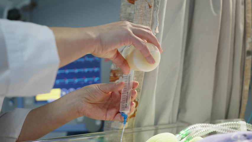 A premature baby in a neonatal intensive care unit receives nourishment from a syringe, donor breast milk. Showcasing the resource in a medical setting.