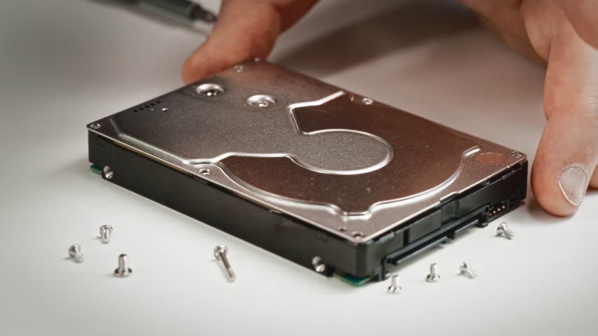 Technician opens hard drive casing, revealing magnetic platters, read write heads, and controller boards. Professional data recovery or repair procedure in progress.