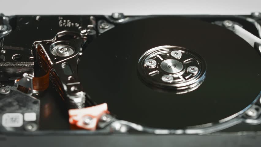 Close-up of an open hard disk drive HDD with spinning platters and visible actuator arm. The image focuses on the inner mechanical components of the storage device
