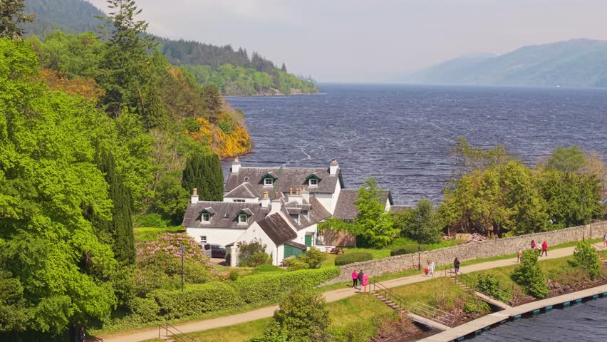 Drone reveal of Loch Ness shoreline at Fort Augustus where the Caledonian Canal flows into the lake, showing serene nature, water, and surrounding greenery