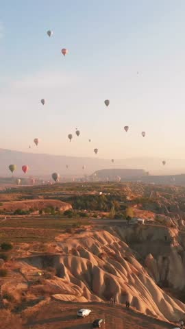 Aerial vertical view Colorful hot air balloons rise over unique Cappadocia arid landscape at sunrise, symbolizing freedom, adventure, bucket list travel, get away, romantic escape, natural wonders