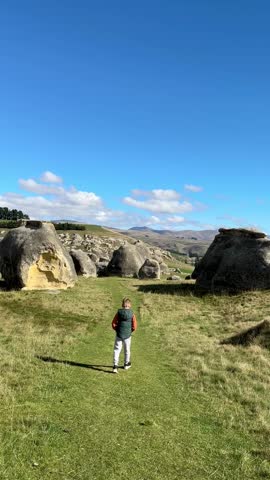 Boy exploring vast rocky landscape under clear blue sky. Elephant Rocks in North Otago, New Zealand. Tourist places. Natural attractions.